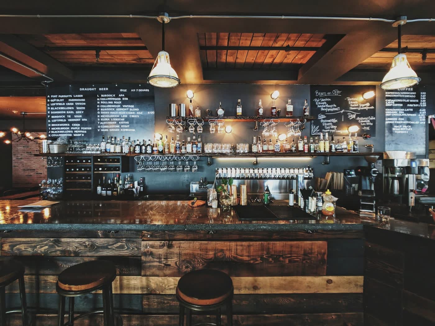 Back-lit bar counter at night, with bottles on lit shelves and a row of empty stools.